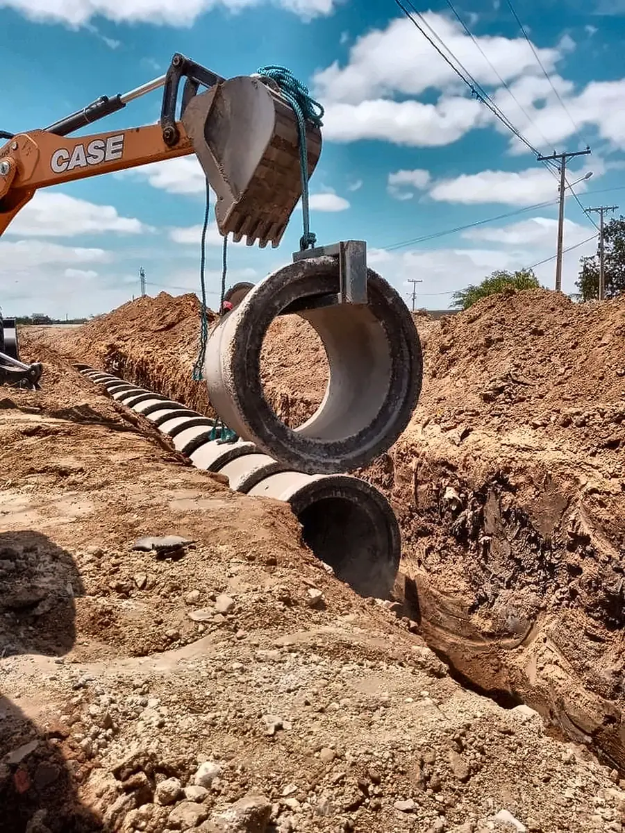 Excavator lowering a large concrete pipe section into a trench